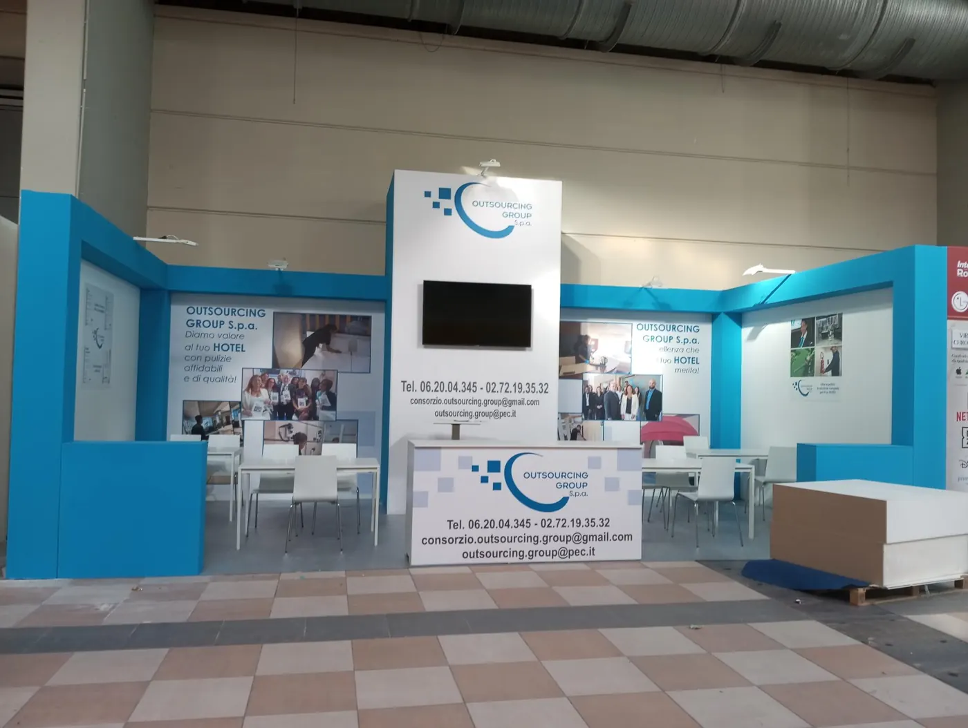 Lo stand Outsourcing Group S.p.A. in fiera: pareti azzurre, banco di accoglienza e tavoli per gli incontri