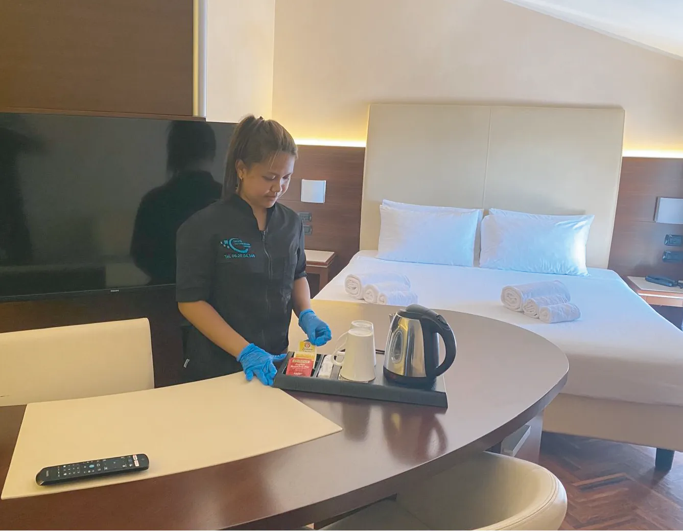 Addetta ai piani in divisa Outsourcing Group prepara il set di cortesia in una camera d’albergo